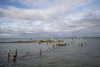 Wooden posts in sea against sky
