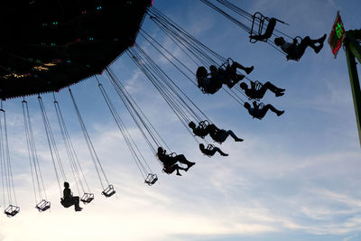 Low angle view of silhouette chain swing ride against sky