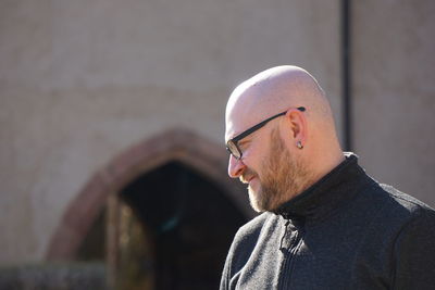 Bearded bald man wearing eyeglasses against building
