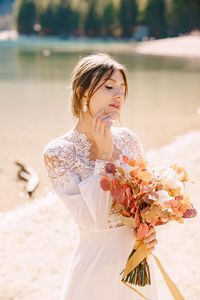 Bride holding bouquet looking away by riverbank