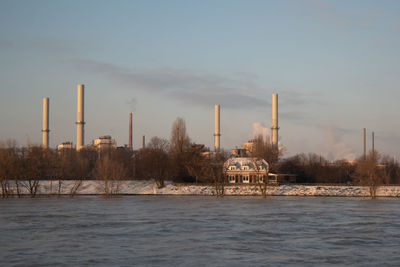 Factory by river against sky