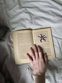 Cropped hand of woman on book over bed