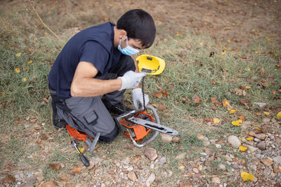 High angle view of man wearing mask holding chainsaw on field