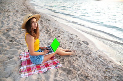 Rear view of woman sitting on sand at beach