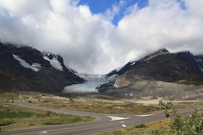 Road leading towards mountains against cloudy sky