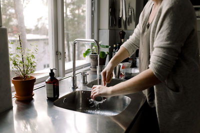 Midsection of woman cleaning cup in kitchen sink at home