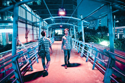 Young men walking on footbridge in city at night