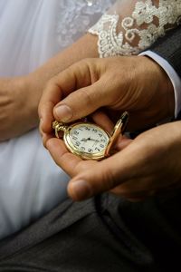 Midsection of groom holding pocket watch by bride