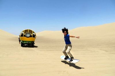 Woman sandboarding on desert against clear sky