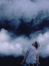 Rear view of teenage boy looking up while sitting against cloudy sky