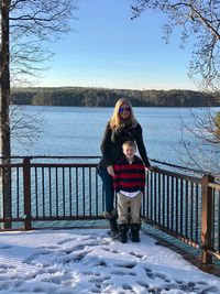 Portrait of smiling woman with son by railing against lake during winter