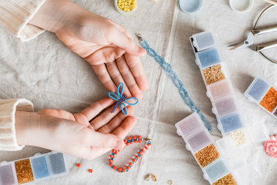 A beaded butterfly in the hands of a girl and items for beadwork on the table. 