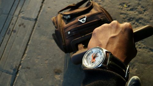 Cropped image of man wearing wristwatch while holding luggage on street