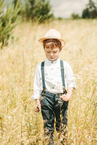 A little farmer is walking in a summer field, a little boy in a straw hat. boy in rubber boots 