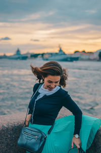 Woman sitting on beach against sky during sunset
