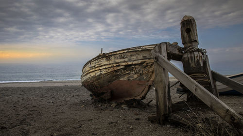 Abandoned boat on beach against sky during sunset