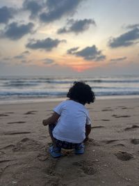 Rear view of woman walking at beach against sky during sunset