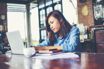 Young woman looking away while sitting on table at cafe