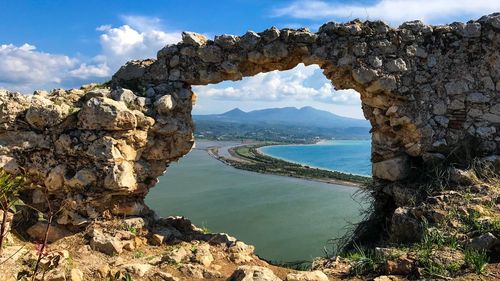 Scenic view of sea and mountains against sky seen through hole