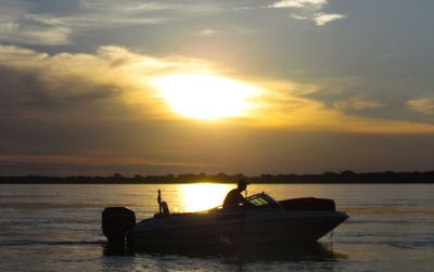 Silhouette people in boat on sea against sunset sky