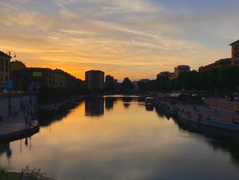 Scenic view of river by buildings against sky during sunset