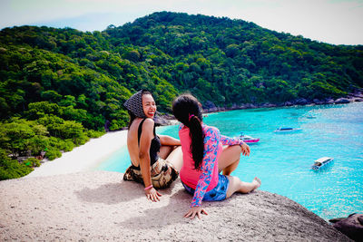 Women sitting on tree by plants against sky