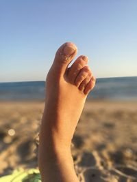 Close-up of woman hand on beach against clear sky