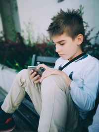 Boy using mobile phone while sitting on bench