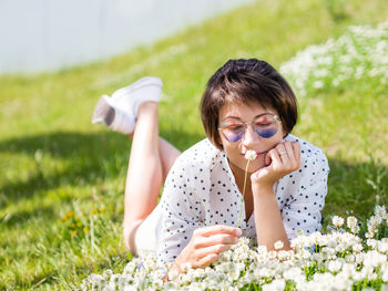 Woman in colorful sunglasses sniffs clover flowers on lawn in urban park. relax outdoors after work.