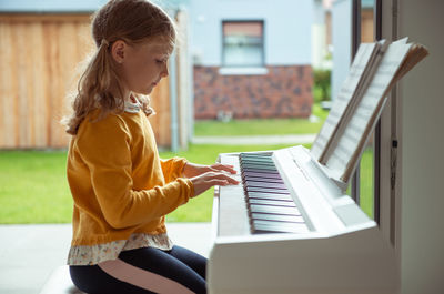 Side view of girl playing piano while siting at home