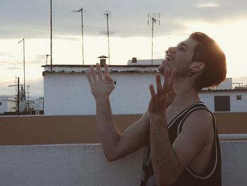 Young man laughing by railing against buildings