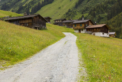 Road amidst field and houses against buildings