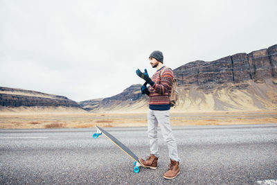 Full length of man standing with skateboard on road against sky