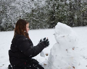 Side view of girl playing with snow by tree