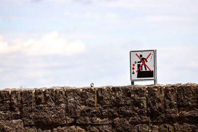 Sign board on rock against sky