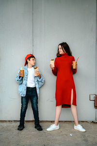 A girl in a red dress and a boy in a denim jacket are holding shawarma and a glass of coffee 