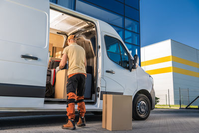 Courier standing by white moving van, opening door. delivering packages to a client