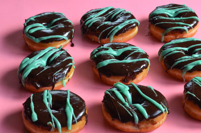 Raised donuts with chocolate frosting with green frosting stripes on pink paper