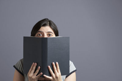 Portrait of woman reading book against gray background