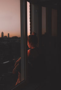 Silhouette man looking through window at sunset