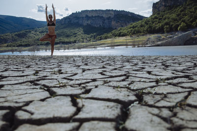 Woman balancing on one leg at the edge of a lake.