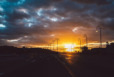 Road by silhouette city against sky during sunset