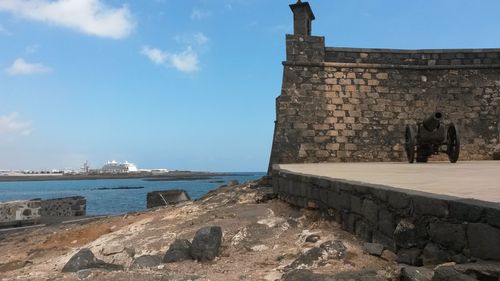 Stone wall by sea against sky in city