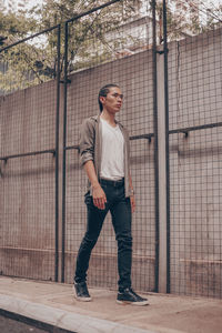 Full length of young man looking away while standing against fence