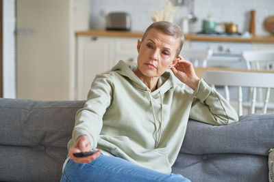 Happy middle aged woman watching tv while sitting on sofa at home