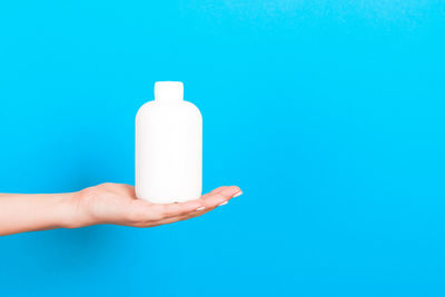 Close-up of hand holding bottle against blue background