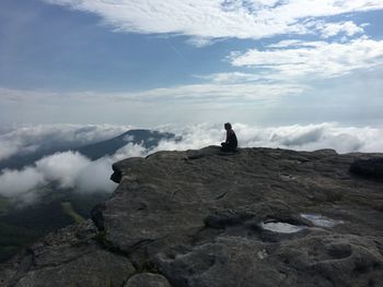 Woman sitting on rock against sky