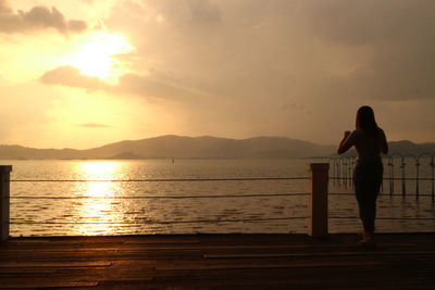 Silhouette woman standing by sea against sky during sunset