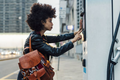 Woman with backpack using ticket machine at electric vehicle charging station