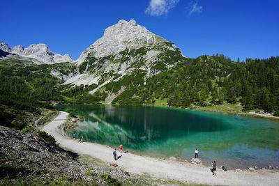 People by lake and mountains against sky